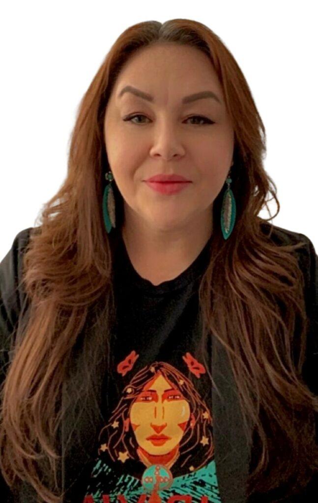 An indigenous woman with long auburn hair and blue beaded earrings.